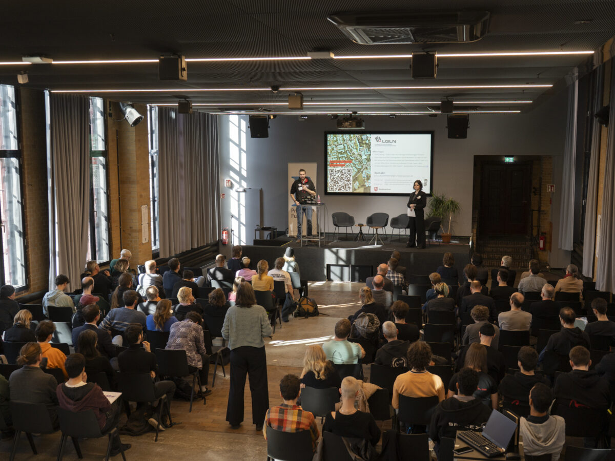 In einem Auditorium hört das Publikum einen Vortrag auf der Bühne.