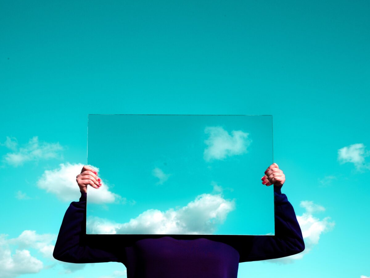 A person holding a mirror infront of their face, mirroring the sky