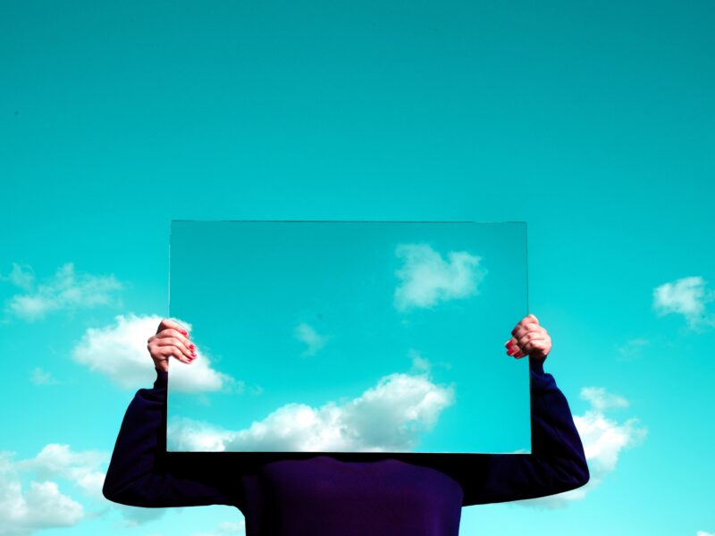 A person holding a mirror infront of their face, mirroring the sky