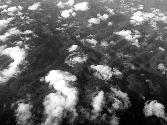 Schwarz-Weiß-Foto eines Gebirges im Bundesstaat Nuevo Leon aus der Vogelperspektive, das teils von Wolken bedeckt ist