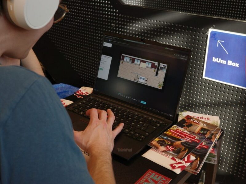 Foto über die Schulter einer Kopfhörer-tragenden Person, die auf einem Laptop ein 2D Spiel bedient.